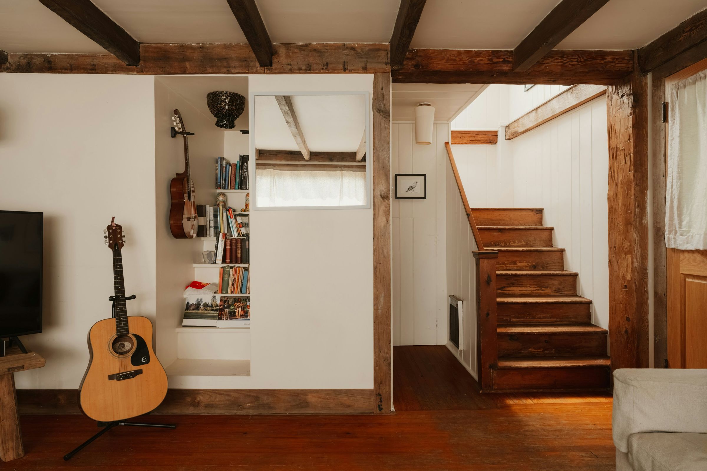 Interior rústico com vigas de madeira à vista e escadas em madeira maciça, semelhante à casa de 1932 onde nasceu o nome Veio.